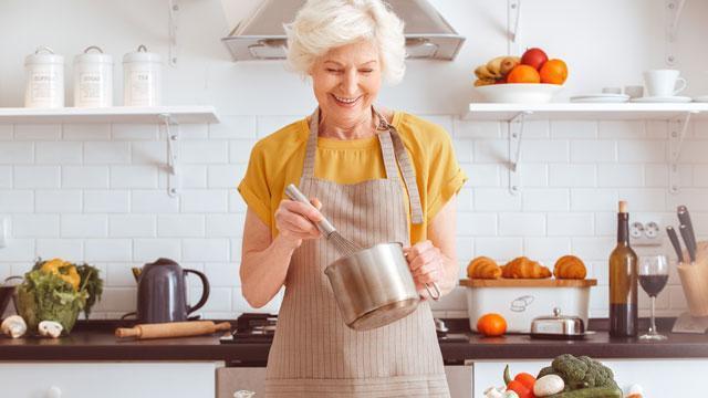 A women cooking in a kitchen while wearing a yellow shirt.