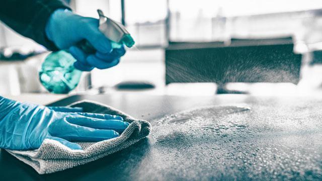A person wearing blue gloves cleaning a table top.