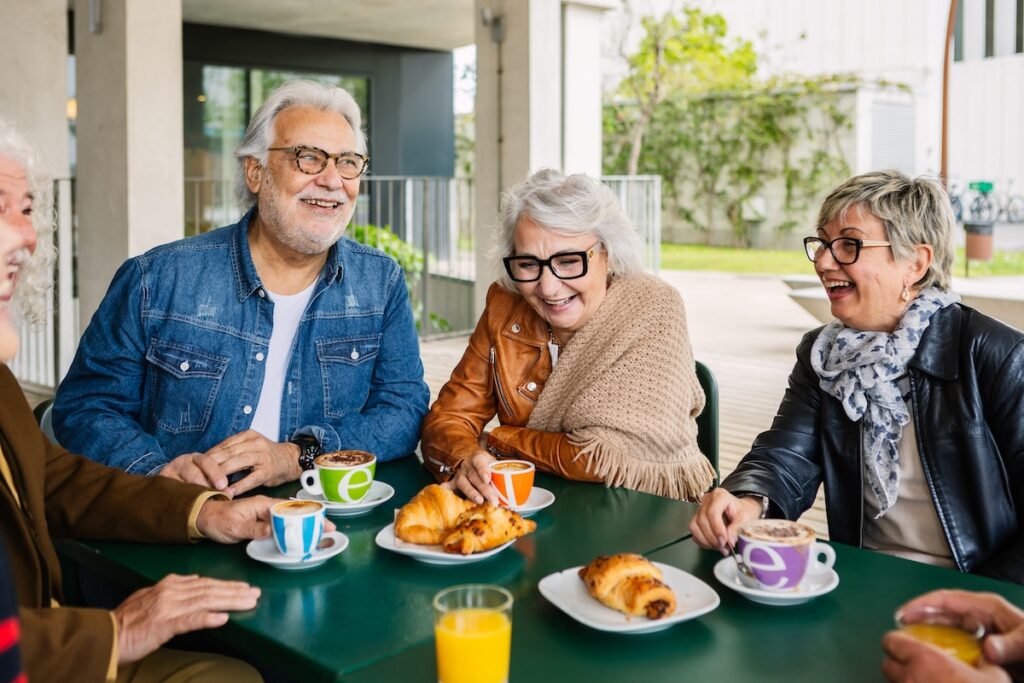 Older adults enjoying coffee and pastries together at a table outside in a social gathering at Hidden Springs community.