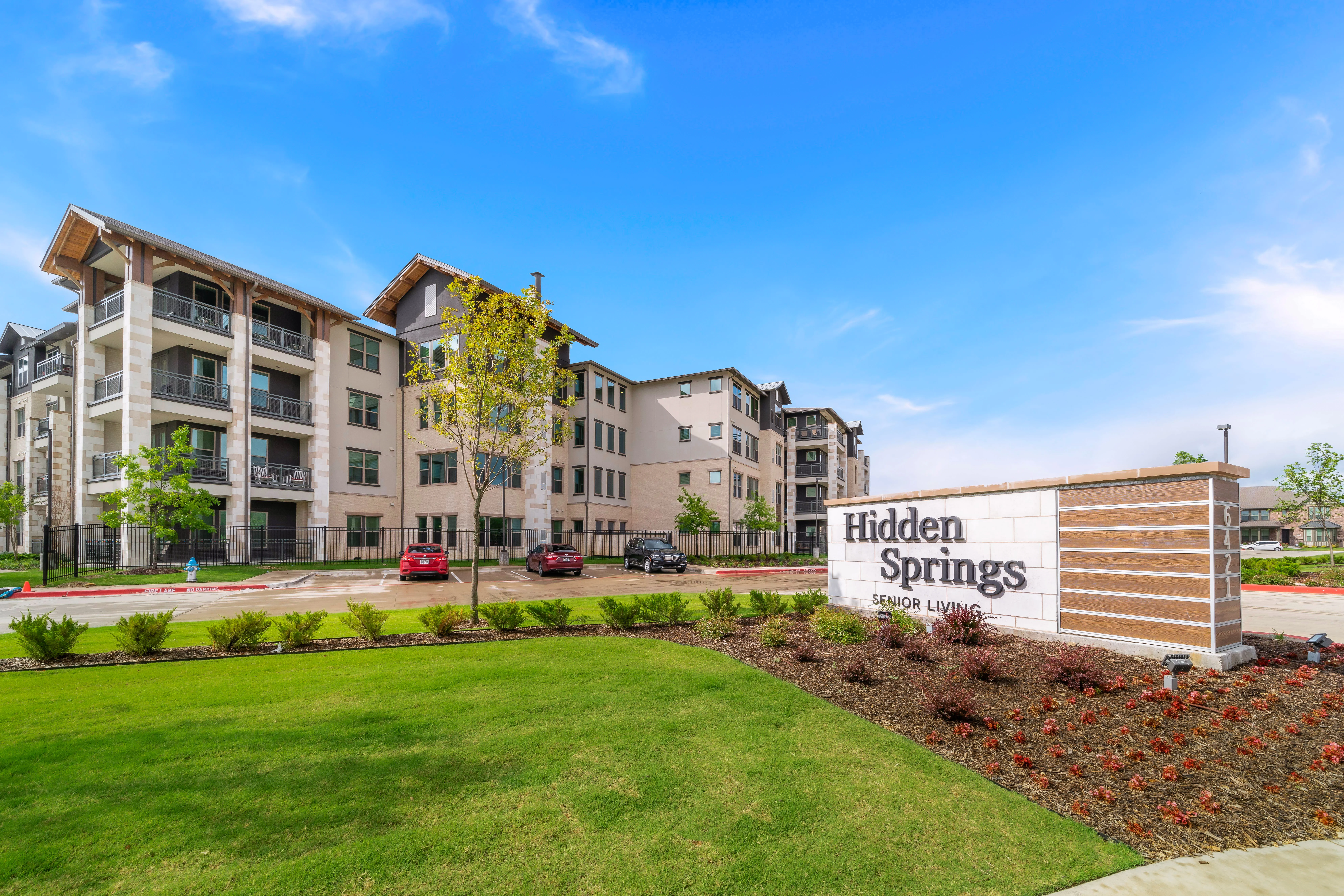 Exterior view of Franklin Hidden Springs senior living community with landscaped lawn and community sign under a blue sky.